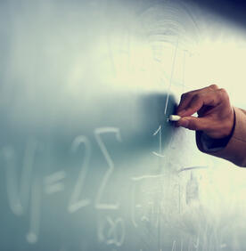 Teacher drawing math symbols on chalk board